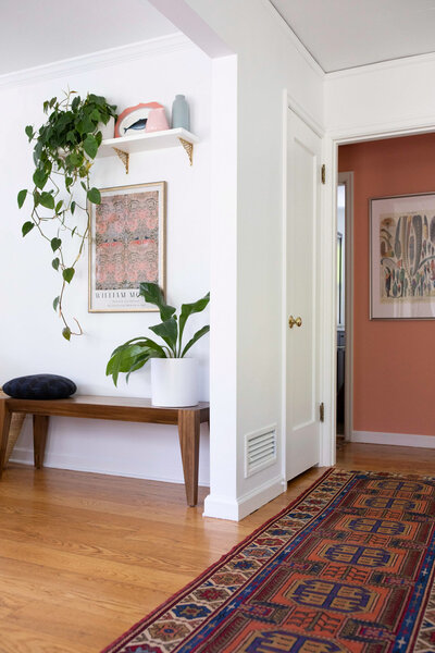 A bright hallway featuring art deco boho interior design with a mix of mid-century and eclectic elements. Includes a bench, potted plants, and a vintage runner rug.