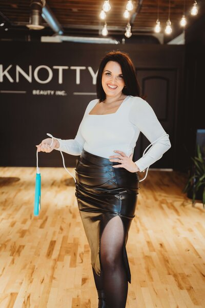 Jess wearing a black skirt and white shirt and turquoise straightener in front of Knotty Beauty signage.