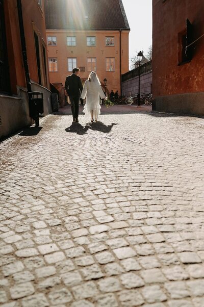 Brudpar går mot solen på kullerstensgata.