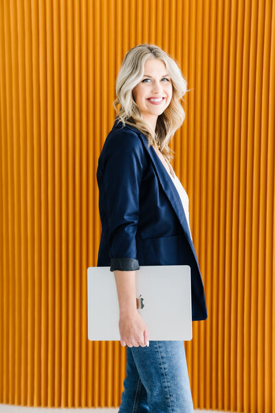 Sarah Klongerbo with one arm in the air holding a magazine and the other arm covering her face