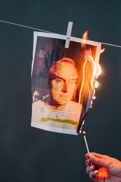 Magazine page hanging by a clothespin being lit on fire with a match