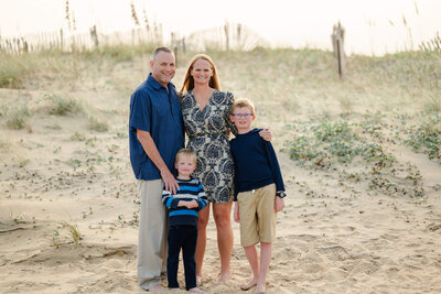 A family of four puts their arms around each other during a family photoshoot on the beach at the Outer Banks.