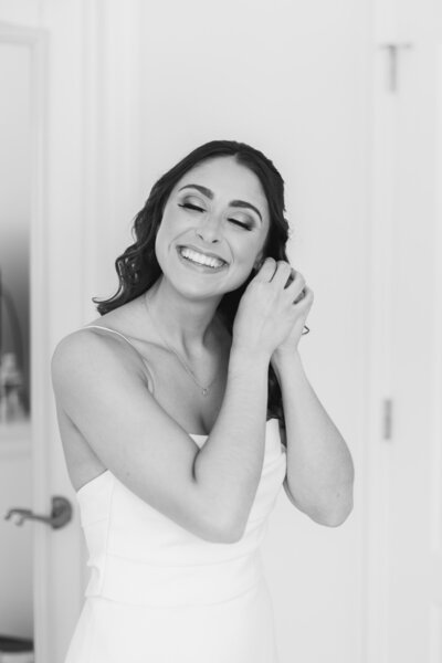 A person in a wedding dress smiling as they put on earrings 