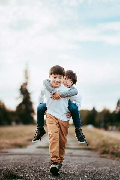 Playful moment of two brothers piggyback riding along a forest trail, captured during a family adventure.