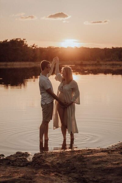 Dansend koppel aan water tijdens zwangerschapsshoot tijdens zonsondergang