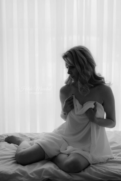 Vrouw zittend op bed met laken voor haar