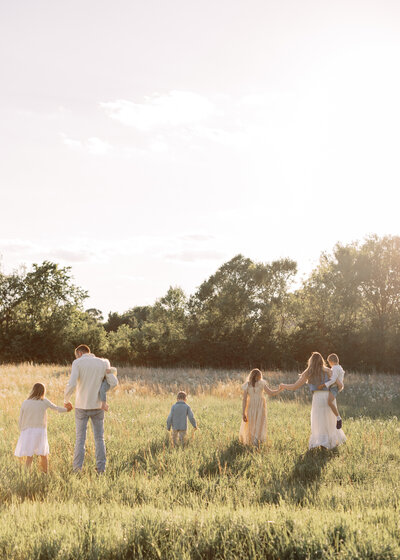 Young family holds hands walking away from bartlesville family photographer in open field