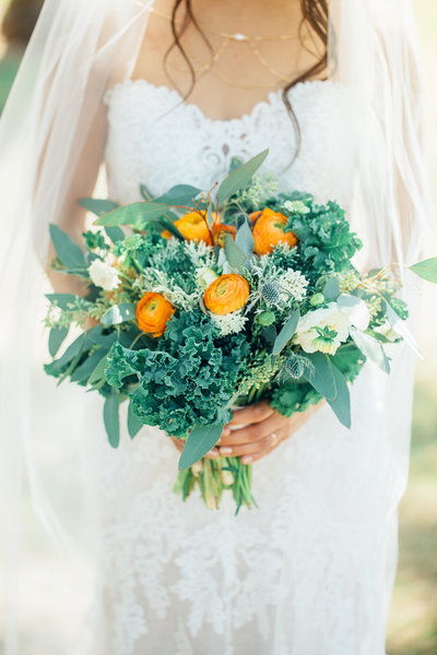 portrait of bride holding kale bouquet with orange accents in wedding dress in Los Angeles