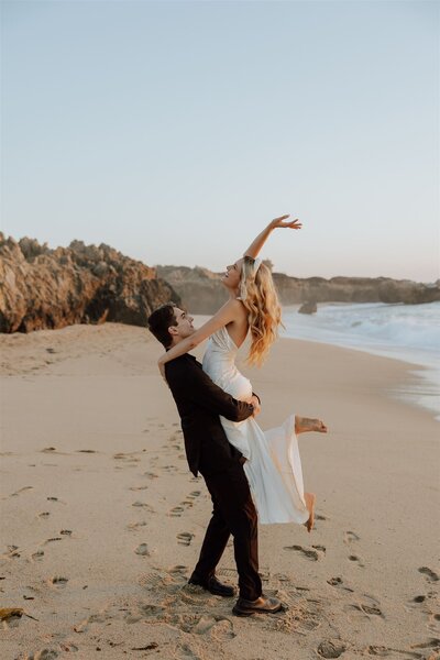 groom spinning bride on a beach with rocky cliffs in the background