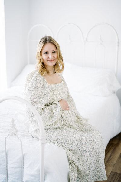 mom sitting on bed with her hand on her belly during maternity photos