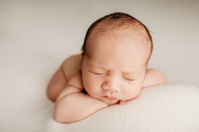 A newborn baby resting his head on his hands during a photoshoot with papakura newborn photographer michelle kelly