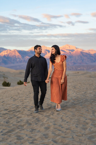 A couple holding hands and smiling while walking in sand