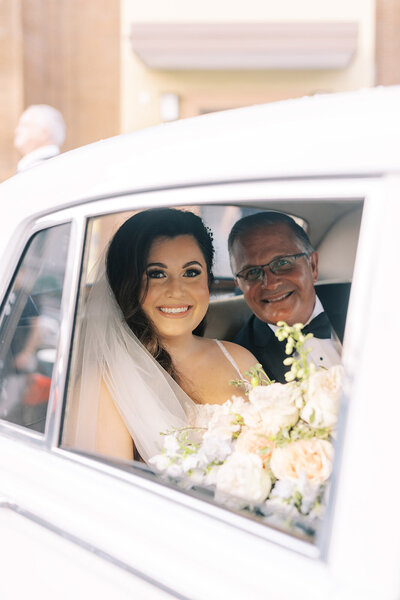 Jenna and father of the bride sitting in classic car on the way to a wedding