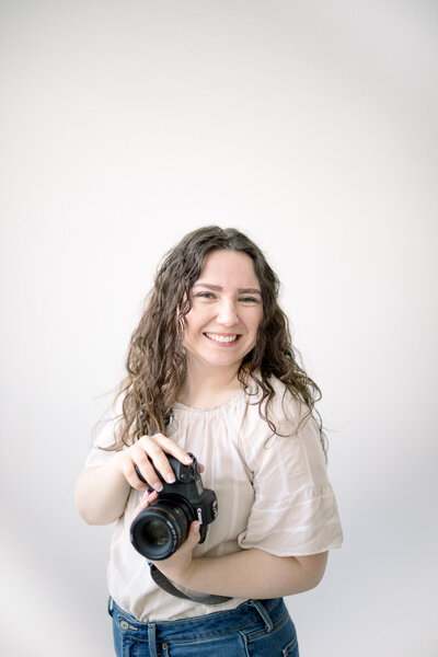 female photographer holding camera and smiling at camera lens taken by spokane wedding photograpeher