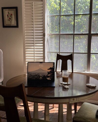 virtual assistant laptop on a wooden dining table by a window