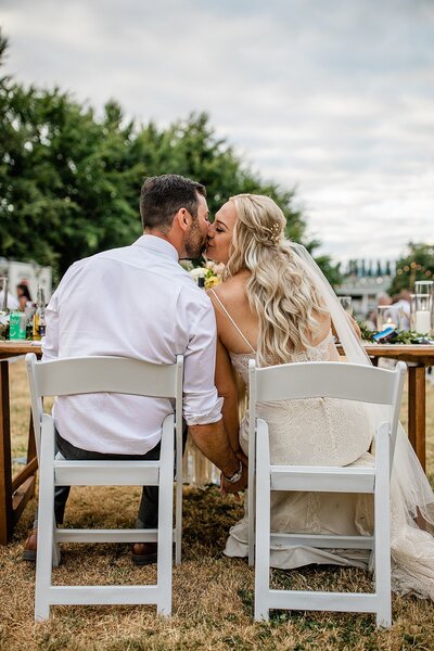 A bride and groom hold hands while facing each other and touching foreheads together. They look very happy and lovingly at each other on their wedding day.
