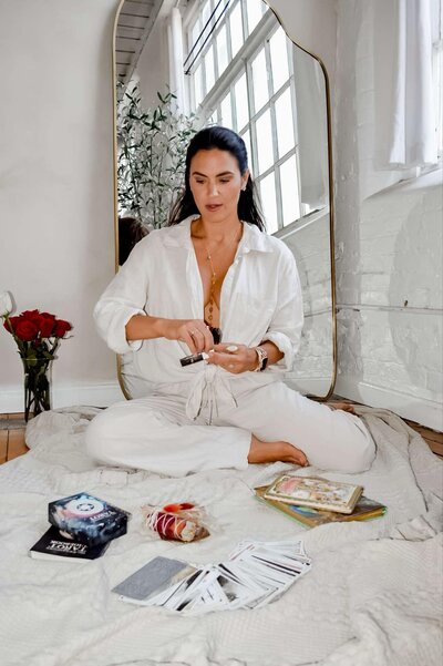 Emily Michele sitting cross-legged on a cozy rug surrounded by journals and oracle cards, representing mindfulness, intention setting, and self-connection.