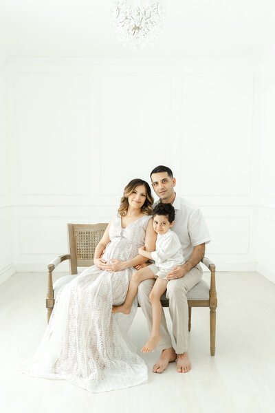 © Reaj Roberts Photography Chandler maternity family sitting on bench in studio under chandelier