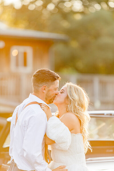 Bride pulling her groom in by his suspenders for a kiss during golden hour.