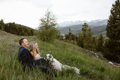 bride and groom sitting on large rocks with lake and mountains in the background