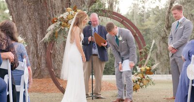 groom smoothing out vow sheet against leg while bride looks on and laughs