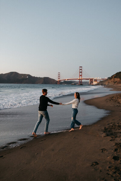 couple dance in the sand at baker beach with the golden gate bridge in the background during sunset
