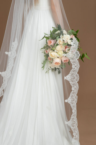 Bride wearing a chapel length veil with lace edge and holding a white and blush bouquet
