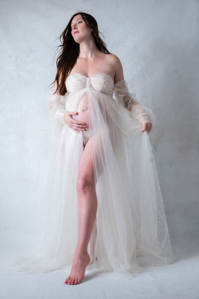 Floral maternity session in studio with mom in flowing open belly gown surrounded by florals