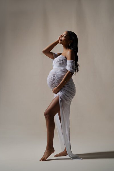 A classic maternity portrait in studio, softly lit against an ivory canvas backdrop. Captured by JPF Galleries, the image reflects the elegance and quiet strength of motherhood.