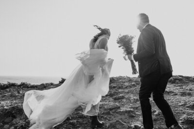 black and white image bride and groom  running on beach