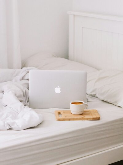 laptop placed on a white bed with coffee nearby
