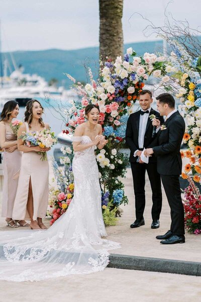 Bride laughing during vows under colorful flower arch, joyful ceremony captured by Toronto photographer