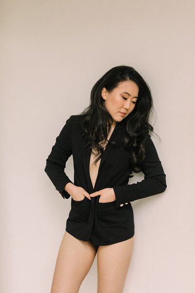 A woman wears only a black blazer for her boudoir session.