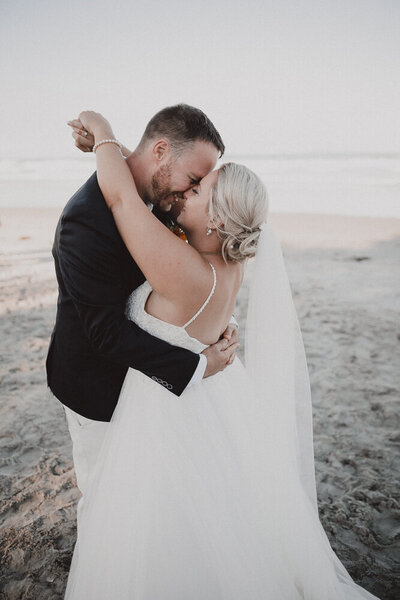 Couple kissing on the beach as newlyweds