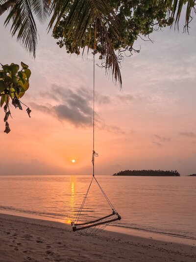 a swing by a beach at sunset in the maldives