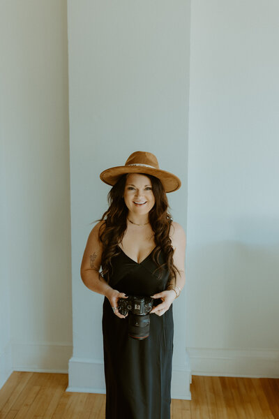 Woman standing smiling at camera holding a camera inside