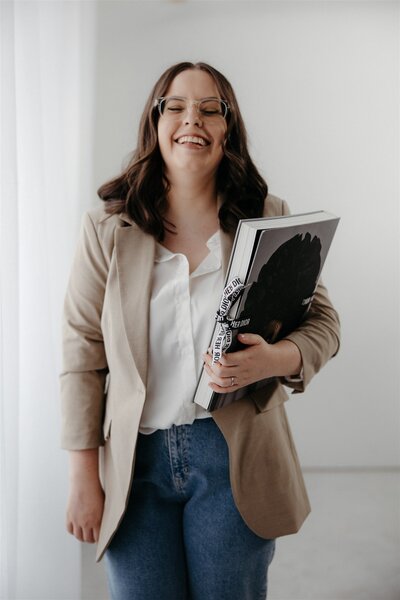Kirsten, founder of KP Virtual Assistance, smiling confidently while holding a large book, representing her approachable and professional support for wedding and lifestyle photographers.