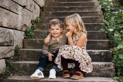 Two smiling children sitting together on outdoor steps, captured by a family photographer in Pittsburgh, PA.