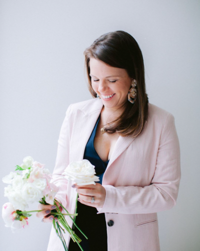 Taylor Batt, owner of Alyson Taylor Events, in a pink blazer looking down at delicate flowers