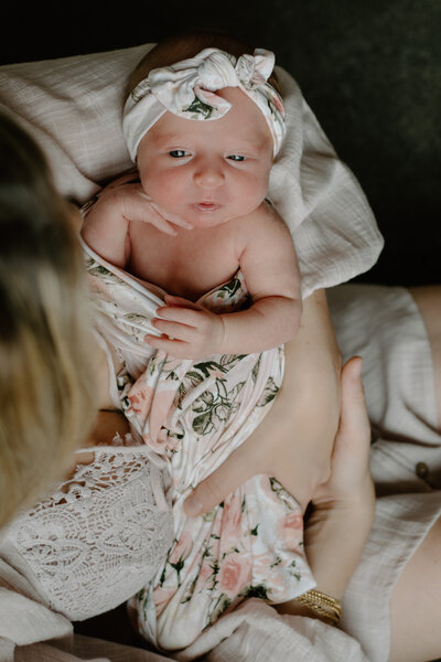 Newborn photo of baby girl wrapped in floral blanket with matching bow while mom is holding her.