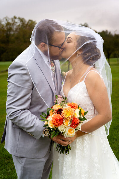 Bride & Groom Kissing on Golf Course with Bouquet underneath her veil