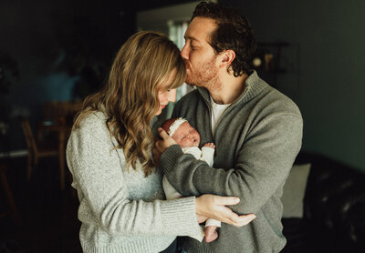 A proud father holds his newborn baby while siblings lovingly pose beside him during a dark-toned, elegant studio session by Duehr Photography in Maple Grove, Minnesota