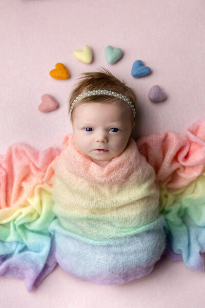 Rainbow baby newborn portrait of a little girl with a rainbow swaddle and hearts