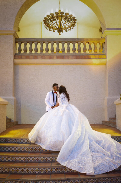 Stunning bride and groom kiss on their wedding day as bride's gown trails down staircase