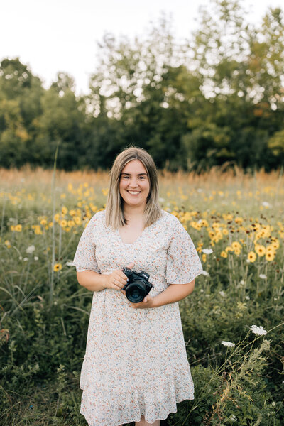 Erin Sage, a detroit area photographer smiling warmly with a camera in hand.