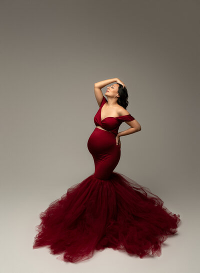 Burgundy mermaid-style maternity gown with off-the-shoulder sleeves and dramatic tulle bottom