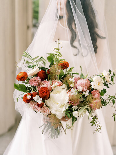 A midsummer nights dream bridal bouquet filled with ranunculus, peonies, garden roses, sweet pea and jasmine vine florals in hues of red, dusty pink, taupe, and green. Designed by Rosemary and Finch in Nashville, TN.