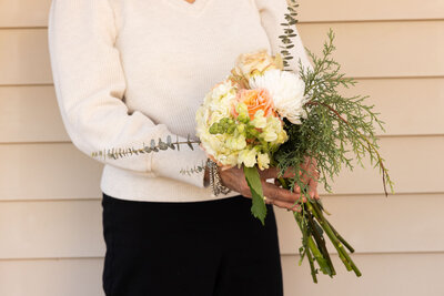 Hand holding a small bouquet with greenery and soft-toned blooms