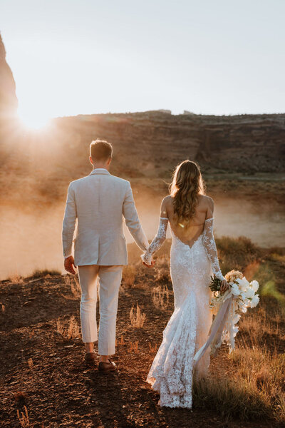 bride and groom holding hands while walking in the desert