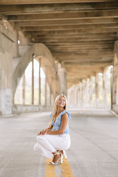 Woman with long, curly blonde hair tilts her head back, eyes closed, in a relaxed pose. She touches her hair with one hand against a black background.